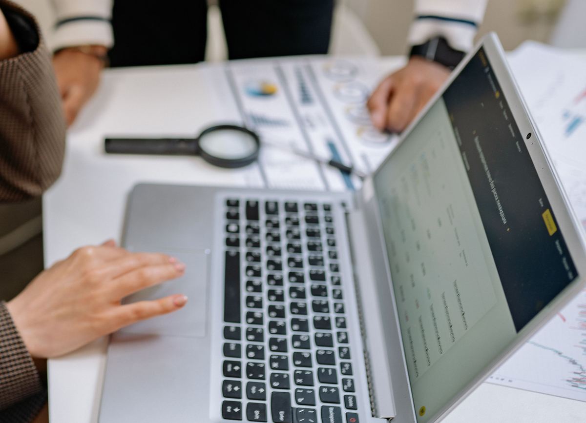 Hands at a laptop keyboard beside printed notes and a magnifying glass