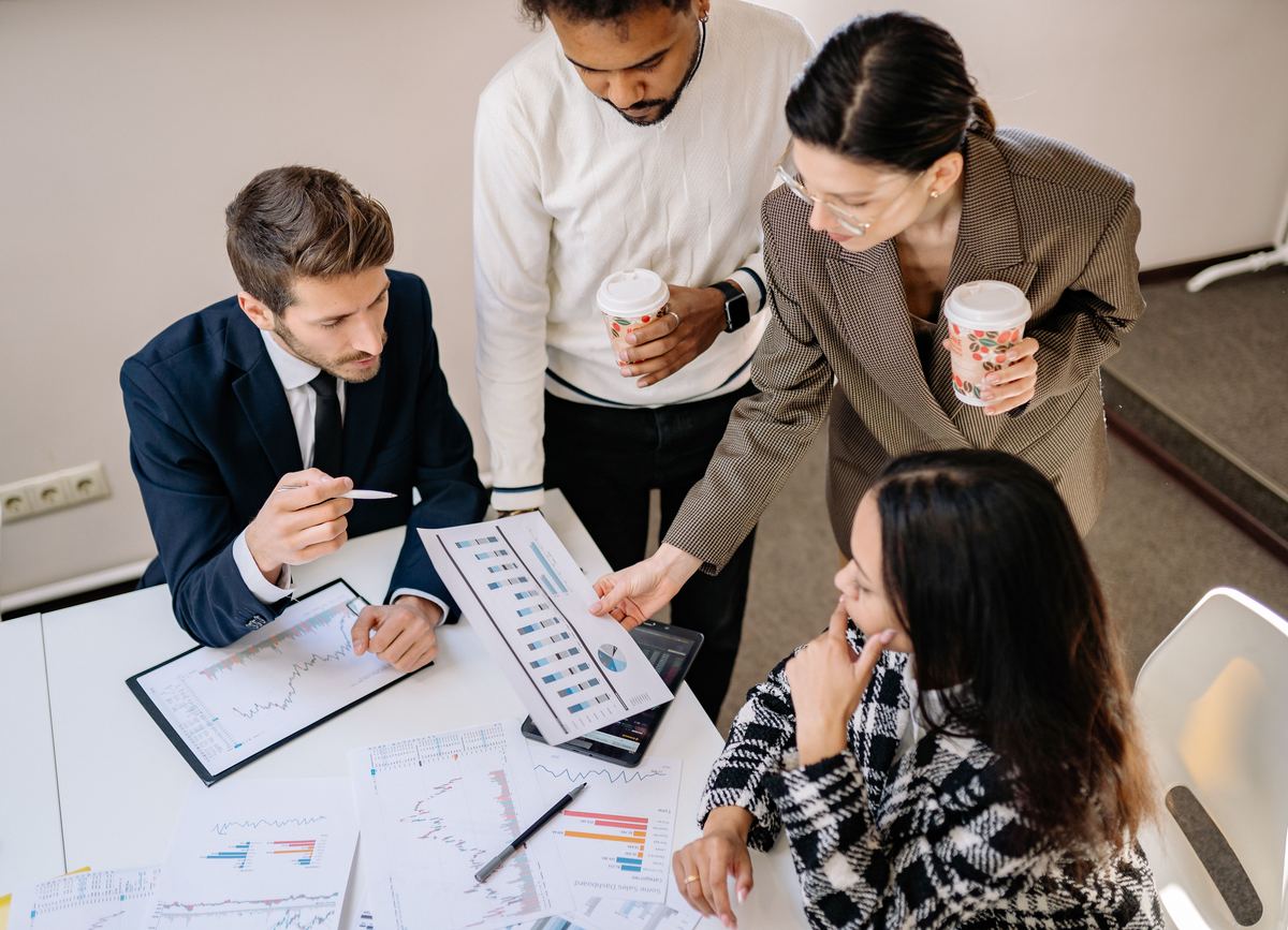 Four colleagues round a table going through printed charts and reports